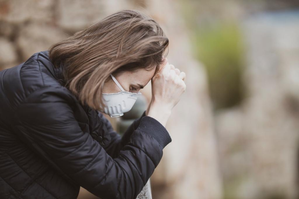 woman with a mask on during the 2020 pandemic with her head in her hands